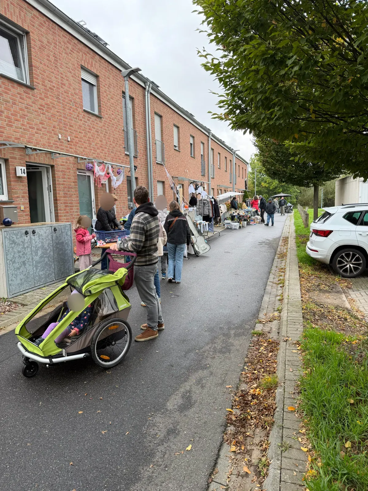 Lange Reihe von Ständen vor Reihenhäusern, ein Mann schiebt einen Fahrradanhänger, an den Hauswänden hängen Halloween-Geister